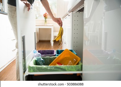 Woman Putting Banana Peel In Recycling Bio Bin In The Kitchen. Person In The House Kitchen Separating Waste. Different Trash Can With Colorful Garbage Bags.