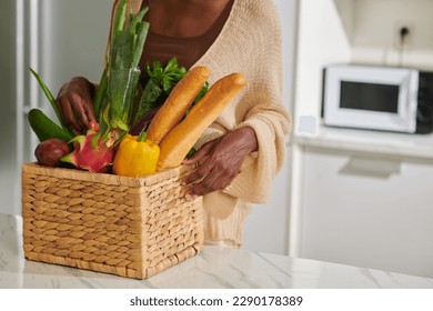 Woman putting basket of fresh groceries on kitchen counter - Powered by Shutterstock