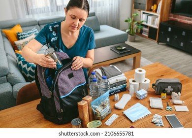 Woman putting cans of food to prepare emergency backpack in living room - Powered by Shutterstock