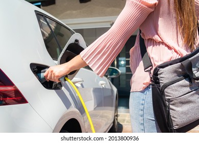 Woman putting a charging plug or charger in a white electric car
