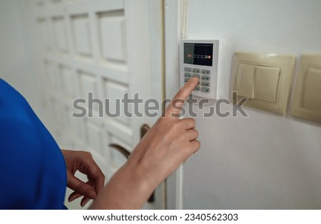 Woman putting code in alarm system panel at home.