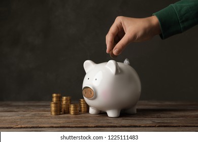 Woman putting coin into piggy bank on table against dark background
