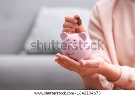 Woman putting coin into piggy bank at home, closeup. Space for text