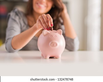 Woman Putting Coin In Piggy Bank, Indoors - Powered by Shutterstock