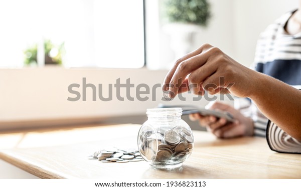 A\
woman is putting coins in a jar with a lot of coins inside, she is\
managing to divide her money to save money and invest it to make it\
grow even more. Concept of saving money and\
investing.