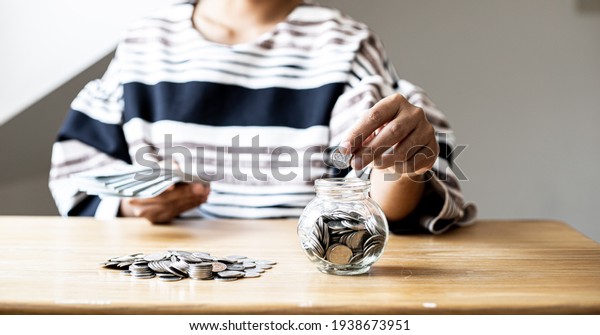 A\
woman is putting coins in a jar with a lot of coins inside, she is\
managing to divide her money to save money and invest it to make it\
grow even more. Concept of saving money and\
investing.