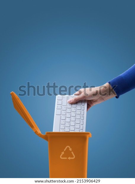 Woman putting a computer keyboard in the e-waste\
trash bin, recycling\
concept