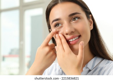 Woman putting contact lens in her eye at home - Shutterstock ID 2215836821