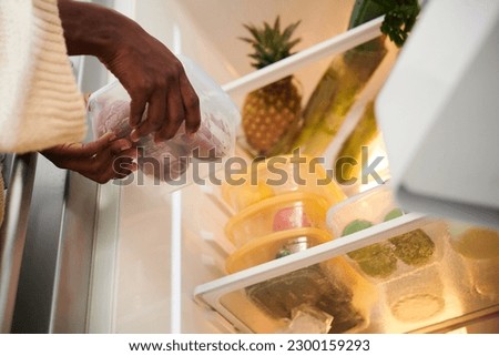Woman putting container with fresh fruits in refrigerator