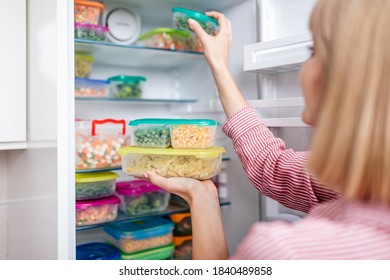 Woman putting containers with frozen mixed vegetables from refrigerator.