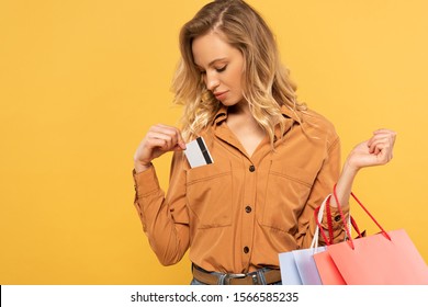 Woman Putting Credit Card In Shirt Pocket And Holding Shopping Bags Isolated On Yellow