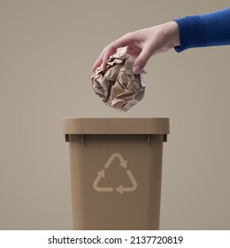 Woman putting crumpled paper in a trash bin, recycling and waste sorting concept