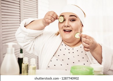 Woman Putting Cucumbers. Smiling Woman Being Contented With Hand-made Beauty Hacks While Covering Her Eyes With Cucumber