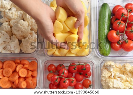 Woman putting cut potato into box and containers with raw vegetables, closeup