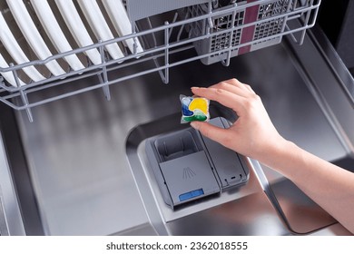 Woman putting detergent tablet into dishwasher.