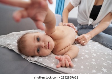 Woman Putting Diaper On Baby, Reaching Out To Camera