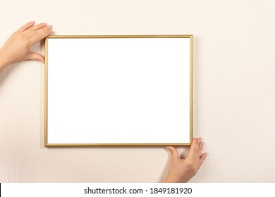 Woman Putting Up Frame Mockup On Wall. Picture Frame Of Hand Is Hanging On The Wall. Young Woman Holding Empty Picture Frame With Copyspace