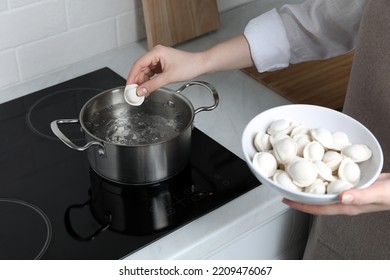 Woman Putting Frozen Dumplings Into Saucepan With Boiling Water On Cooktop In Kitchen, Closeup