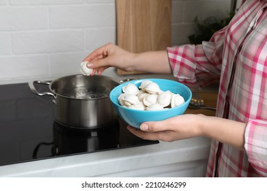 Woman Putting Frozen Dumplings Into Saucepan With Boiling Water On Cooktop In Kitchen, Closeup