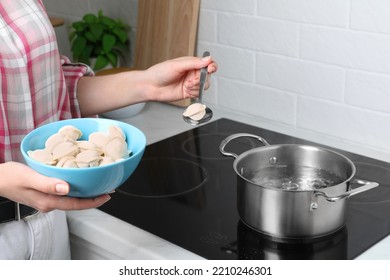 Woman Putting Frozen Dumplings Into Saucepan With Boiling Water On Cooktop In Kitchen, Closeup