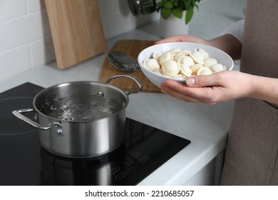 Woman Putting Frozen Dumplings Into Saucepan With Boiling Water On Cooktop In Kitchen, Closeup