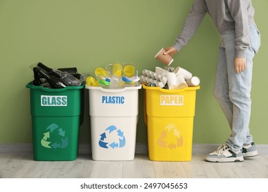 Woman putting garbage into full trash bins with different types of waste near green wall. Recycling concept - Powered by Shutterstock