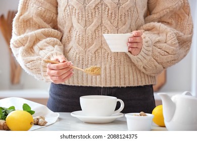 Woman putting ginger powder into cup on table in kitchen - Powered by Shutterstock