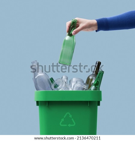 Woman putting a glass bottle in the trash bin, separate waste collection and recycling concept