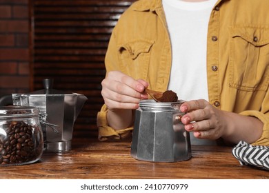 Woman putting ground coffee into moka pot at wooden table, closeup - Powered by Shutterstock