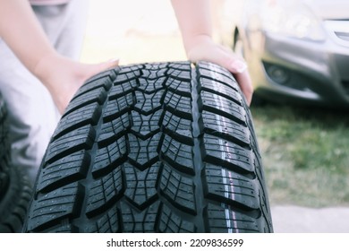 Woman Putting Hand On New Wheel Tire. Female Holding A Tire And Standing Next To A Piles Of Tires. Auto Car Repair Service