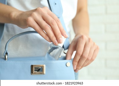 Woman Putting Hand Sanitizer In Purse On Light Background, Closeup. Personal Hygiene During COVID-19 Pandemic