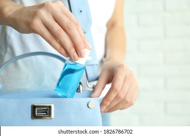 Woman putting hand sanitizer in purse on light background, closeup. Personal hygiene during COVID-19 pandemic