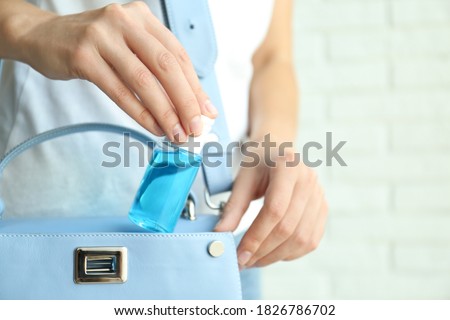 Woman putting hand sanitizer in purse on light background, closeup. Personal hygiene during COVID-19 pandemic