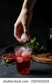 Woman Putting Ice Cube Into Glass With Healthy Cranberry Juice On Dark Background