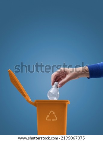 Woman putting an incandescent lightbulb in the waste bin, recycling and environmental care concept