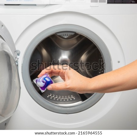 Woman putting laundry detergent capsule into washing machine indoors, closeup.Colorful laundry eco gel in capsule. Washing clothes.The concept of washing and cleanliness