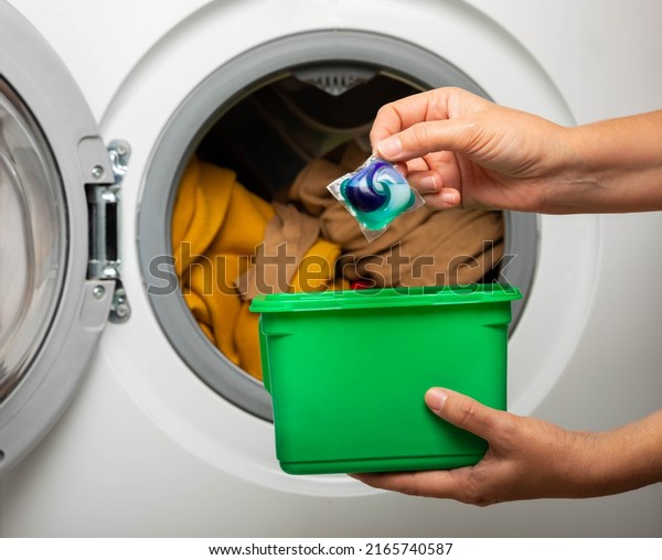 Woman putting laundry\
detergent capsule into washing machine indoors, closeup.Colorful\
laundry eco gel in capsule. Washing clothes.The concept of washing\
and cleanliness