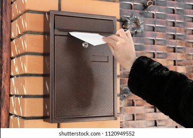 Woman Putting Letter In Mailbox Outdoors