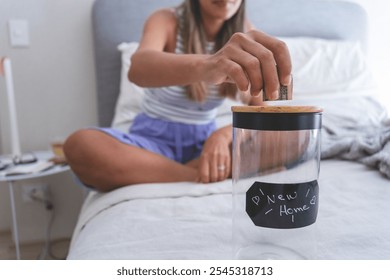 A woman is putting money into a jar labeled New Home. New home concept. - Powered by Shutterstock