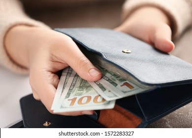 Woman putting money into wallet at brown table, closeup