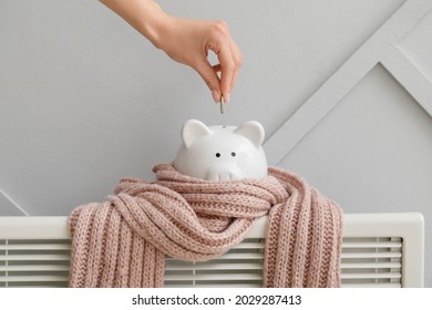 Woman putting money in piggy bank on radiator. Concept of heating season