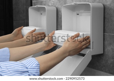 Woman putting new fresh paper towels into dispenser in bathroom, closeup