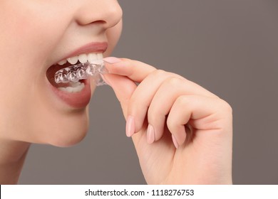 Woman Putting Occlusal Splint In Mouth On Grey Background, Closeup