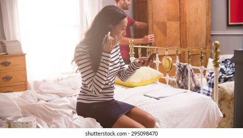 Woman Putting On Make Up And Man Getting Dressed In Bedroom