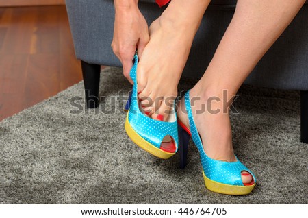 Woman putting on a pair of trendy blue shoes with cut out toes as she sits on an armchair in indoors in a fashion accessories and footwear concept