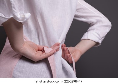 Woman putting on pink apron against grey background, closeup - Powered by Shutterstock