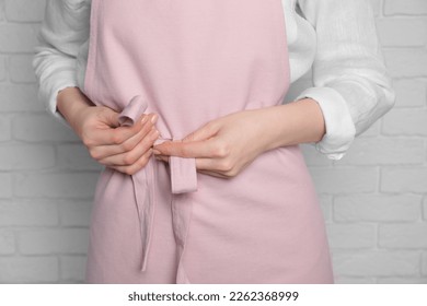 Woman putting on pink apron against white brick wall, closeup - Powered by Shutterstock