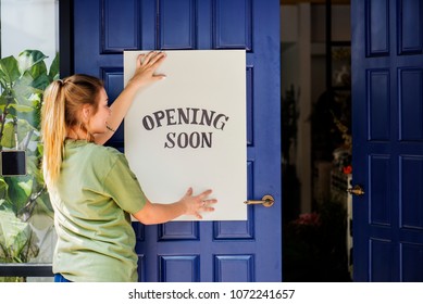 Woman putting on store opening soon sign
