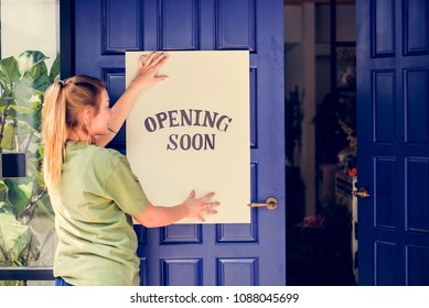 Woman Putting On Store Opening Soon Sign