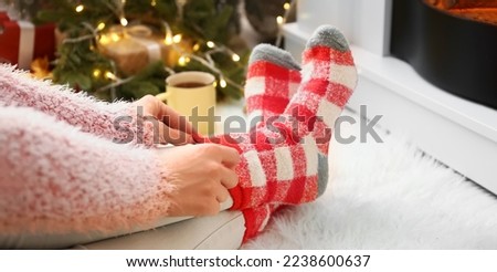 Woman putting on warm socks while sitting near fireplace at home on Christmas eve, closeup